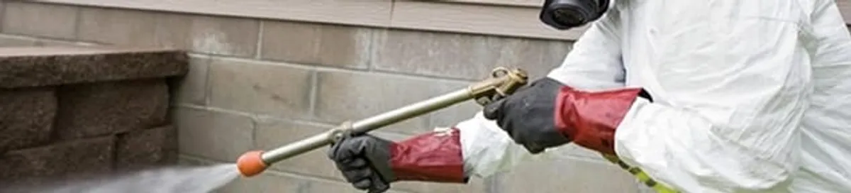 Pest control technician applying exterior insect treatment along a home foundation in Dayton, OH