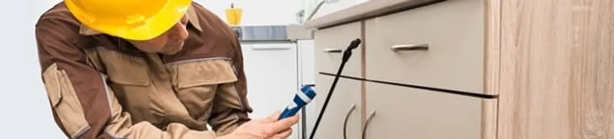 Roach exterminator applying treatment under kitchen cabinets in Dayton, OH