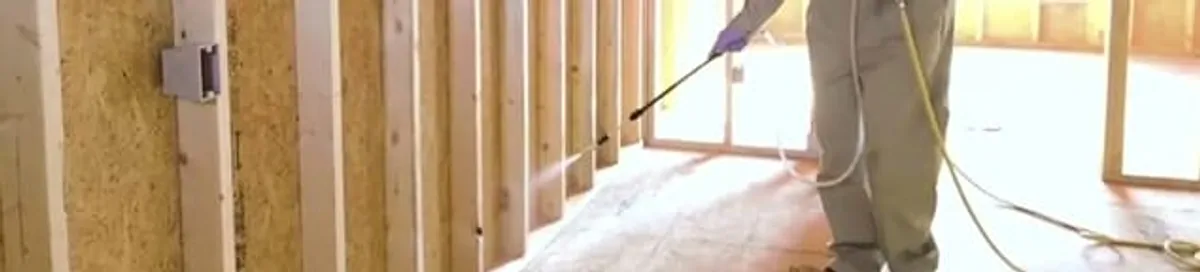 Termite treatment technician applying spray along framing and unfinished walls in Dayton, OH